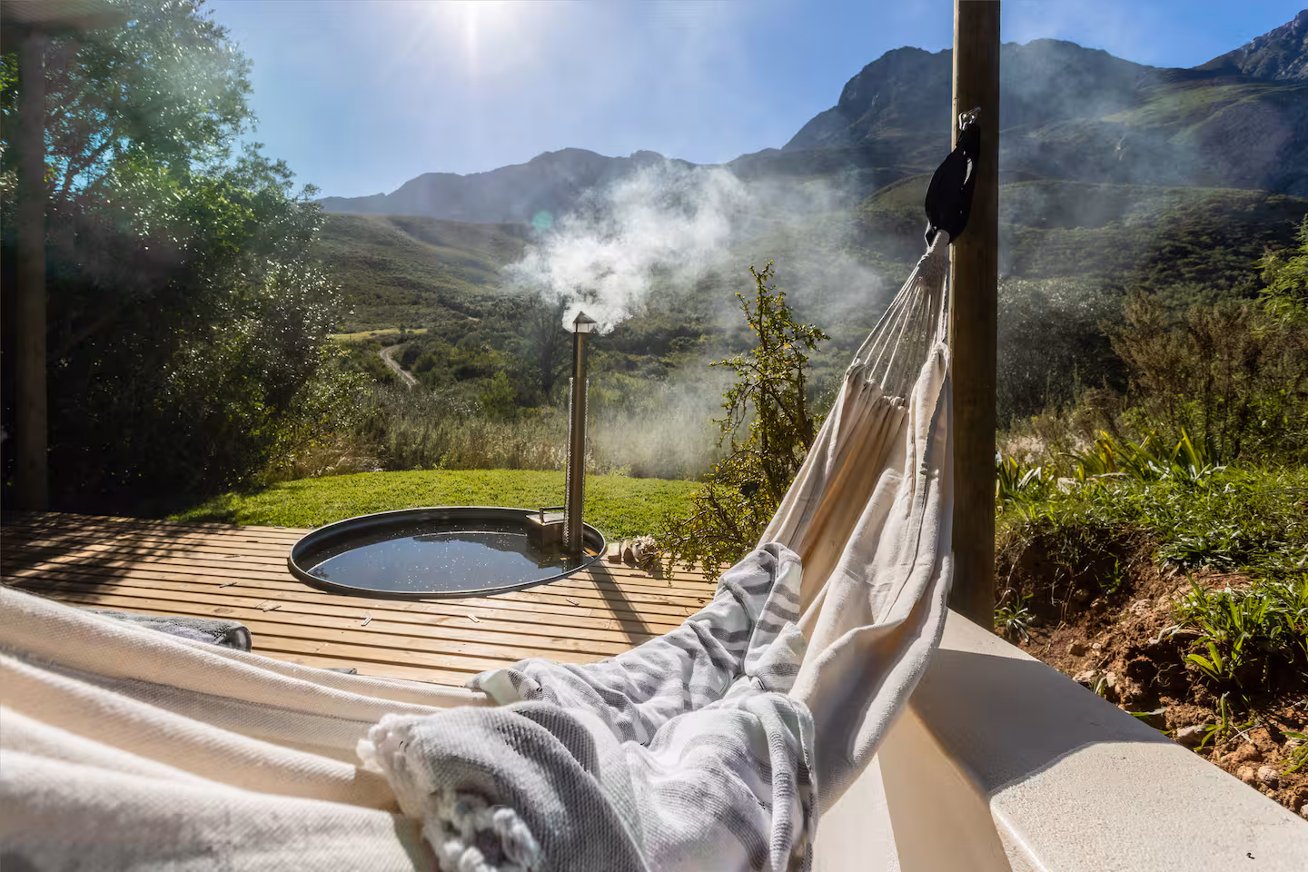 A hammock and wood-fired hot tub on the deck at Wilde Als in Robertson, mountains beyond